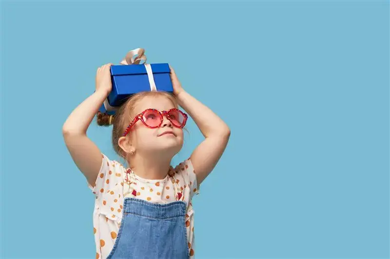 niña-sonriente-con-gafas-corazon-y-regalo-azul-sobre-la-cabeza